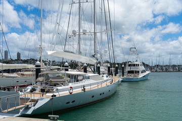 Fototapeta premium A sleek luxury yacht moored at Viaduct Harbour with the modern Auckland CBD skyline and clear blue sky in the background.