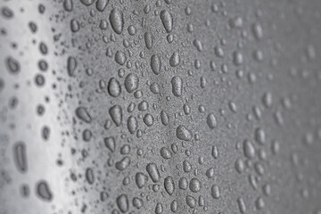 Water droplets aligned in vertical pattern on monochrome surface suggesting gravity flow and moisture movement