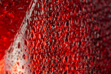 Dramatic water droplets on glass surface illuminated with intense red lighting creating abstract texture and reflection