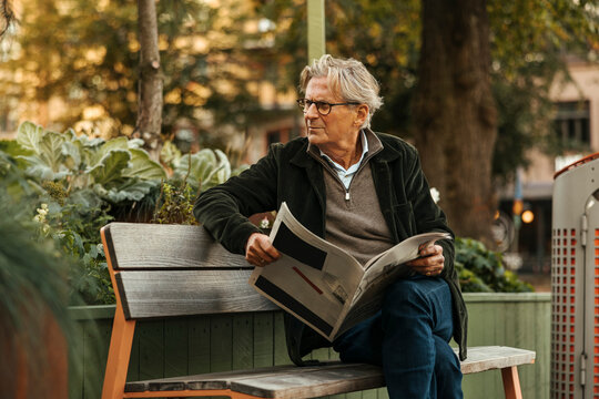 Senior man looking away holding newspaper in hand while sitting on bench