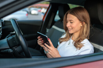 Young woman drives car and uses portable touchscreen computer