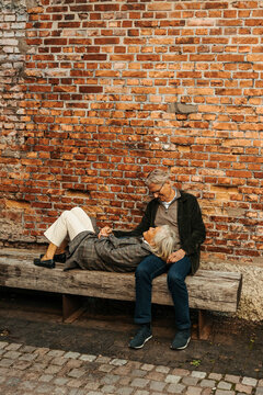 Carefree senior woman lying down on man's lap at bench near brick wall