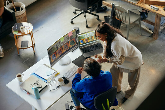 High angle view of female tech professional talking with male colleague working on desktop PC in startup office
