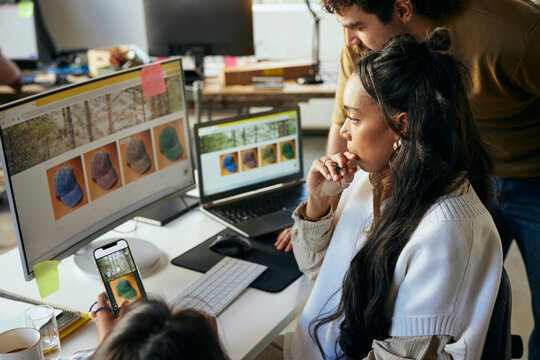 Focused female programmer working with colleagues on desktop PC in startup office