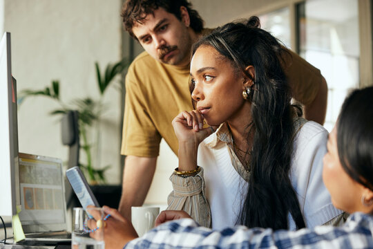 Concentrated female programmer working with colleagues on desktop PC in startup office
