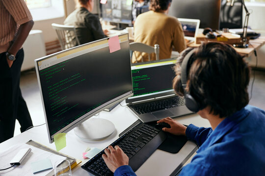 High angle view of young male programmer coding on desktop PC in tech office