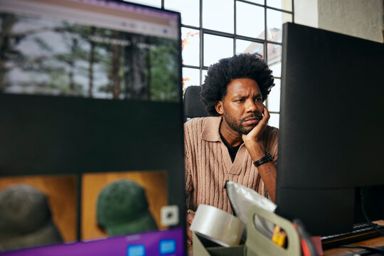 Focused curly haired male tech professional leaning on elbow while working in startup office