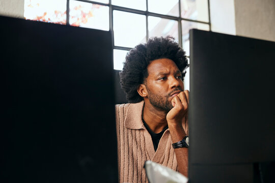 Curly haired male tech professional leaning on elbow while working in startup office