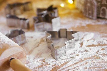Baking gingerbread cookie cutters, wooden rolling pin, and flour are messily spread on rustic kitchen table. Process of cooking festive traditional Christmas sweets, bakery