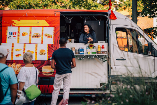 Smiling young saleswoman talking with male customer from food truck