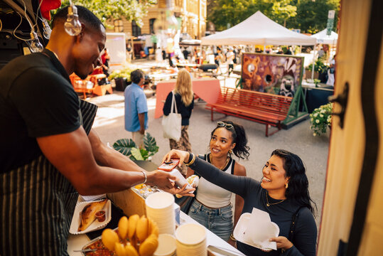 Smiling salesman holding credit card reader while female customer tapping smart phone on it at food truck