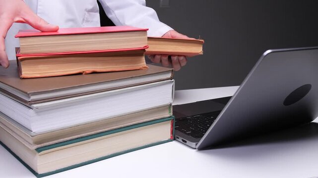 Doctor hands adding old academic books to a stack beside a modern laptop, illustrating the blend of traditional medical knowledge and digital technology in healthcare education and research