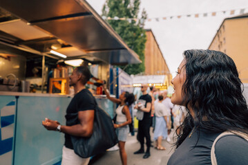 Long haired young woman looking at friend ordering food on street