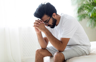 Obraz premium Impotence Concept. Upset Pensive Young Indian Man Sitting On Bed At Home, Worried Eastern Man Suffering Erectile Dysfunction Problem, Resting In Bedroom, Thinking About Health Issues, Copy Space