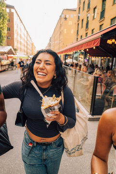 Happy young woman holding french fries walking with friends on street
