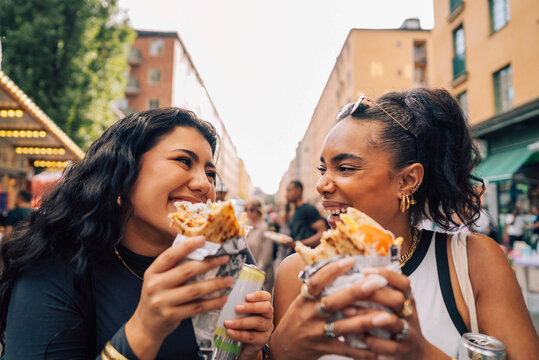 Happy female friends eating wrap sandwich at food festival