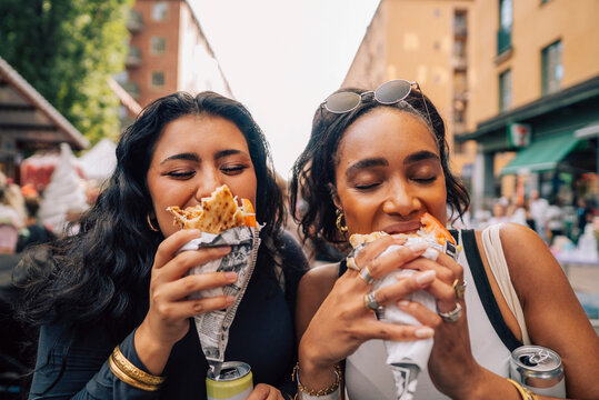 Multiracial female friends indulging in wrap sandwich at food festival