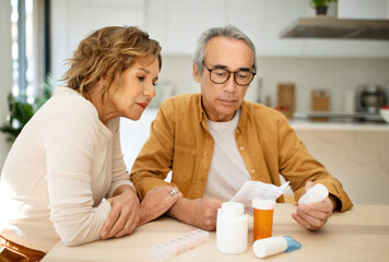 Nutritional supplement. European senior spouses reading prescriptions for new pills or vitamins, sitting at table in kitchen interior, copy space