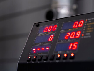 Emissions testing device showing numerical readings during automotive diagnostic procedure in professional garage