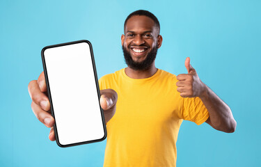New cool mobile app. Funky African American guy demonstrating cellphone with empty screen, showing...