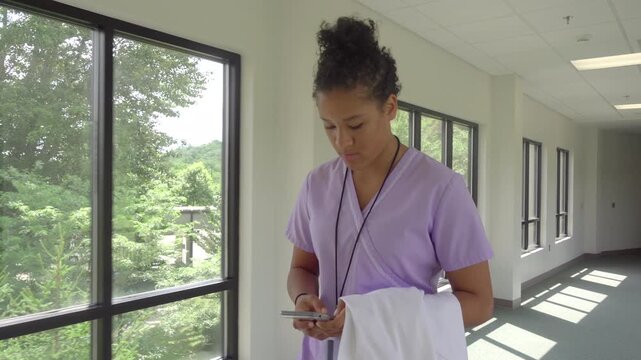 African American Nurse Walking Down Hospital Hallway Typing on Smartphone