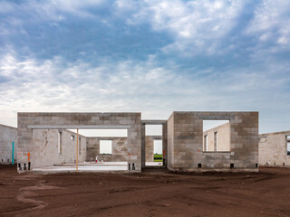Concrete shell of a single-family house under construction, with framed views through front entrance (middle) and garage (left), in a suburban development on a cloudy morning in southwest Florida