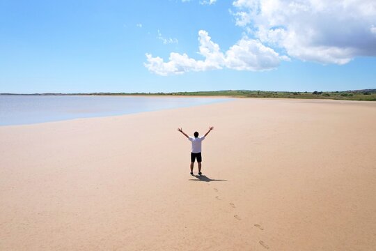Man raising arms on sandy beach, limnos island, greece alyki salt lake