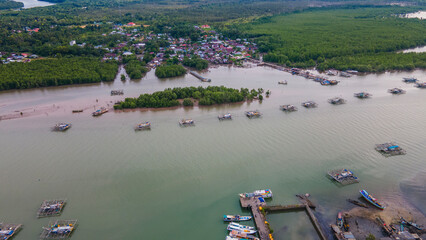 Aerial view of the Cerucuk River estuary flowing into the open sea in Tanjung Pandan, Belitung, Indonesia. Features lush mangrove forests, lines of floating fish cages, and a coastal fishing village.