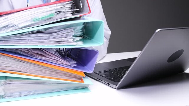 Doctor engaging with a large stack of patient files and documentation, highlighting the heavy administrative burden and potential for burnout in the medical profession