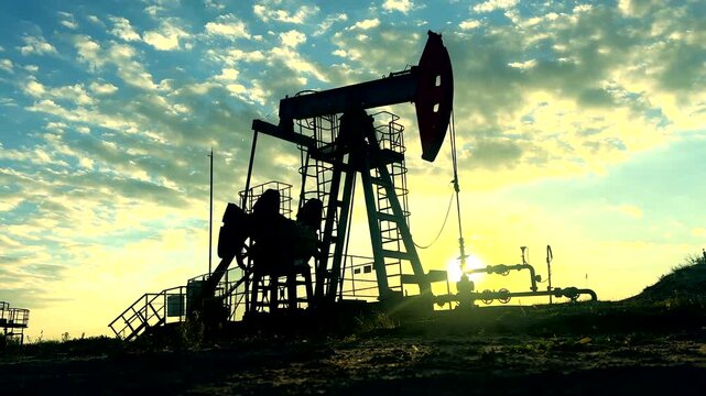 Crude pump jack on sunrise in oil field. Oil Pump Jack Operates on Beautiful Sunset at Oil Field in Industrial Area. Oil drill rig, drilling derrick in oilfield. Crude petroleum industry. 