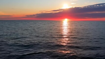 The sun sets over the calm ocean, creating a vibrant reflection on the water's surface. This ocean and sunset combine to form a tranquil and beautiful evening scene.