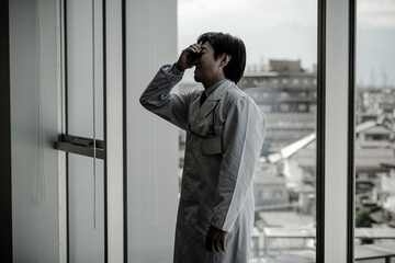 A middle-aged male doctor holding his head (medical error, depressed, worried, overworked,...