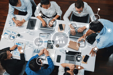 A dynamic overhead view showcasing a diverse team engaged in a collaborative meeting with laptops, charts, and digital symbols representing connectivity and teamwork. Amity