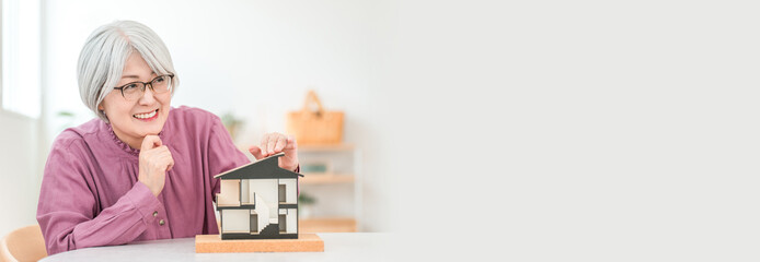 A gray-haired senior woman holding a house model (home building, custom-built house, own home)