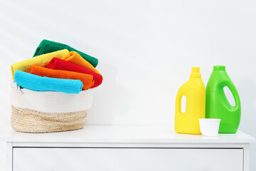 Laundry basket with towels and bottles of detergent on dresser near white wall indoors, space for text