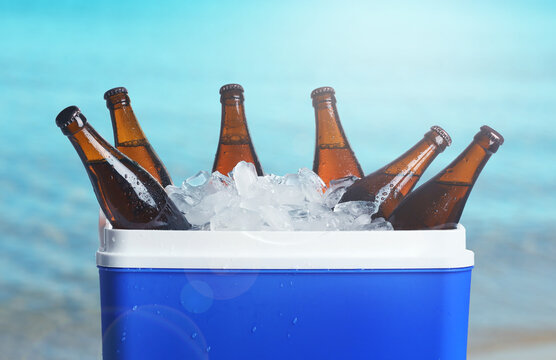 Bottles of beer and ice in cooler box near sea. Refreshing summer drink