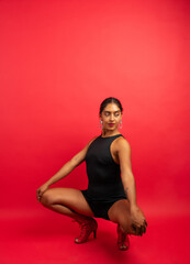 Woman performing a dance pose wearing a black leotard and red high heels