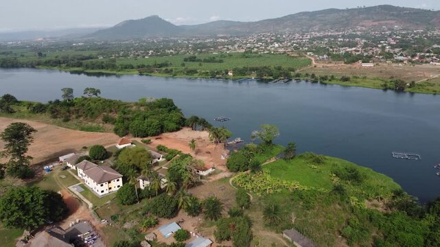 Aerial drone footage of Ghana, Africa, serene lake surrounded by mountains. Traditional boats across the water near a local village, with views near the Right to Dream Football Academy