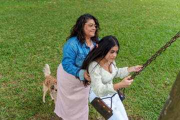 Latina mom supporting her teenage daughter on a swing during a park day