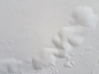 White painted wall with severe bubbling and peeling due to moisture. Close up of water damaged wall surface with large paint blisters. Abstract texture of swollen, damaged white paint and plaster.