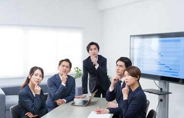 オフィスで会議するビジネスマン男女が考える