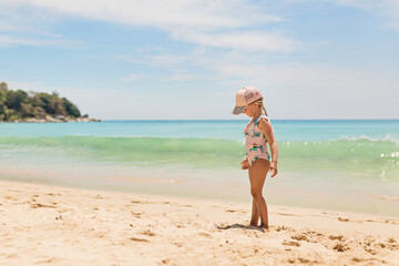Young girl wearing swimsuit and cap standing on sandy beach near ocean