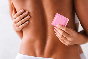 Woman hugging her partner from behind while holding a pink condom package in her hand to show responsibility in a romantic relationship