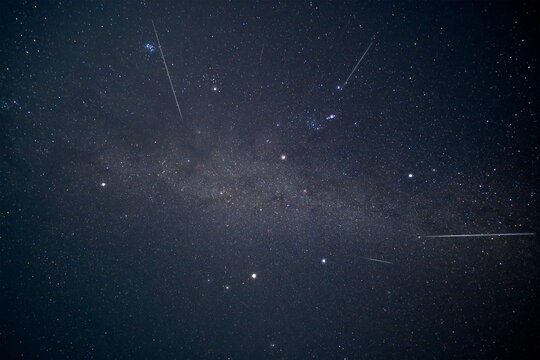 A stunning long exposure of Geminid meteor shower streaks across the Winter Hexagon asterism and a faint Milky Way in a clear dark night sky. Breathtaking astronomical event.