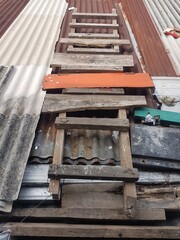 Makeshift wooden ladder resting vertically on a corrugated roof. Simple rustic construction from salvaged wood and planks. Temporary access to a metal roof surface.