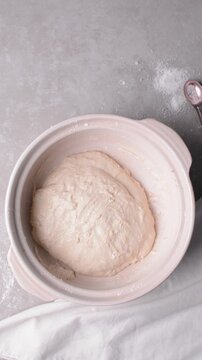 Overhead view of focaccia dough being folded and shaped on a cement countertop, top view of homemade focaccia bread dough in a claypot, process of making focaccia 