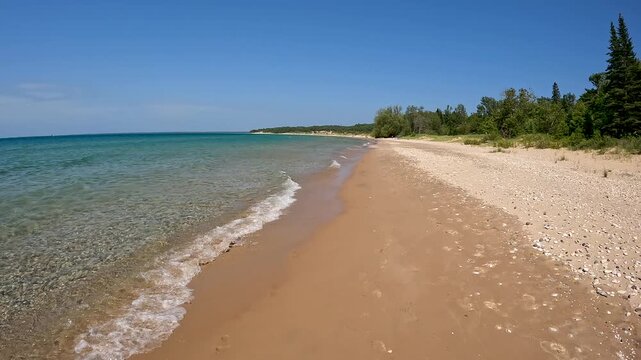 Stunning Natural Beauty on the Sandy Shore of Lake Michigan. Moving backwards along the coast. Waves crash onto the sandy beach with rocks. Wilderness State Park in Northern Michigan, USA.