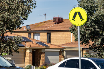 Houses beside a suburban street in Australia, near a public car park with a pedestrian crossing warning sign. Residential infrastructure, road safety awareness, neighborhood living