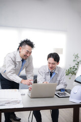 Fototapeta premium パソコンを見ながら笑顔でポシティブに話す作業着のビジネスマン2人 製造業などのdxやit化のイメージ 