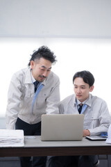 Obraz premium Two businessmen in work clothes talking while looking at a computer Image of DX and IT adoption in manufacturing and other industries